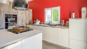 Una cocina moderna con armarios blancos, una pared de acento roja, un ventanal grande y una lámpara colgante.