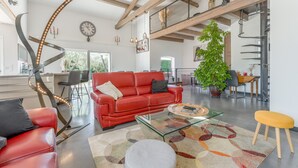 Un salón amplio con un sofá rojo, una mesa de centro de vidrio y una planta grande.