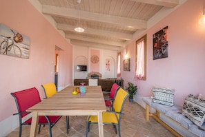 Un comedor con una mesa de madera, sillas rojas y amarillas, un sofá con cojines estampados y un televisor en la pared.