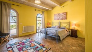 A bedroom with a bed, a nightstand, a lamp, a radiator, a window with curtains, and a colorful rug.