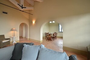 Un vaste espace de vie comprenant un canapé, une table à manger et des chaises, une porte en arc de cercle et une petite table avec une lampe.