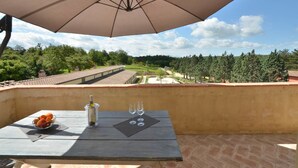 A balcony with a table, an umbrella, and a view of a vineyard. - Hotel Apartment "Quercia" with Shared Pool & Wi-Fi (Trequanda)