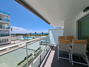 A balcony with a view of a pool and beach, two striped chairs, and a whiteboard.