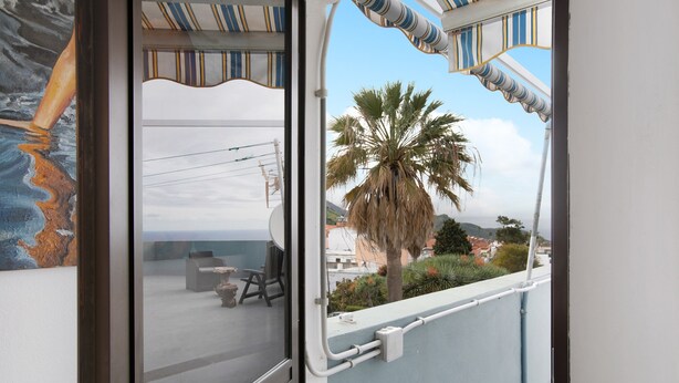 A balcony with a view of the sea, a palm tree, and a building in the background. - Vacation Studio 'La Zotea' with Mountain View and Wi-Fi (Tegueste)