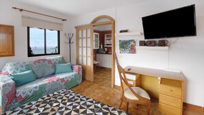 A room with a sofa, a desk, a chair, a television, and a view of the outside. - Vacation Studio 'La Zotea' with Mountain View and Wi-Fi (Tegueste)