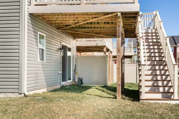 A residential building with a covered patio area, a wooden staircase, and a visible door.