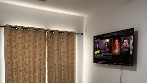 Une chambre à coucher avec un lit, des rideaux, un ventilateur de plafond et un téléviseur fixé au mur.