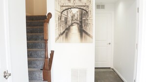 Un couloir avec un escalier, une pancarte de bienvenue et une œuvre d’art représentant un pont, accrochée au mur.