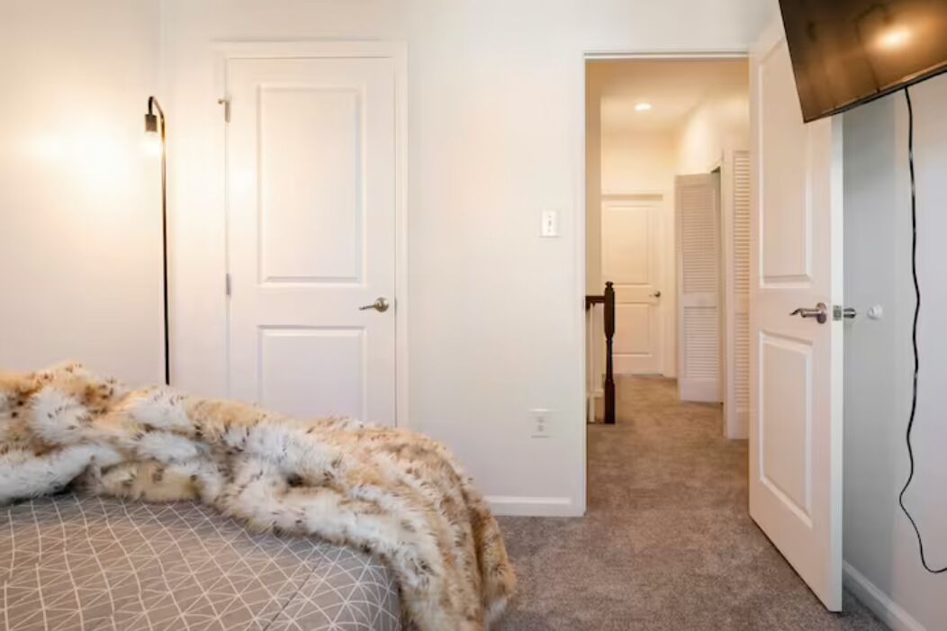 Une chambre avec un lit, une porte blanche, un couloir et un téléviseur fixé au mur.
