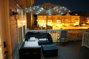 A wooden deck with outdoor seating, a covered area with string lights, and a building in the background.