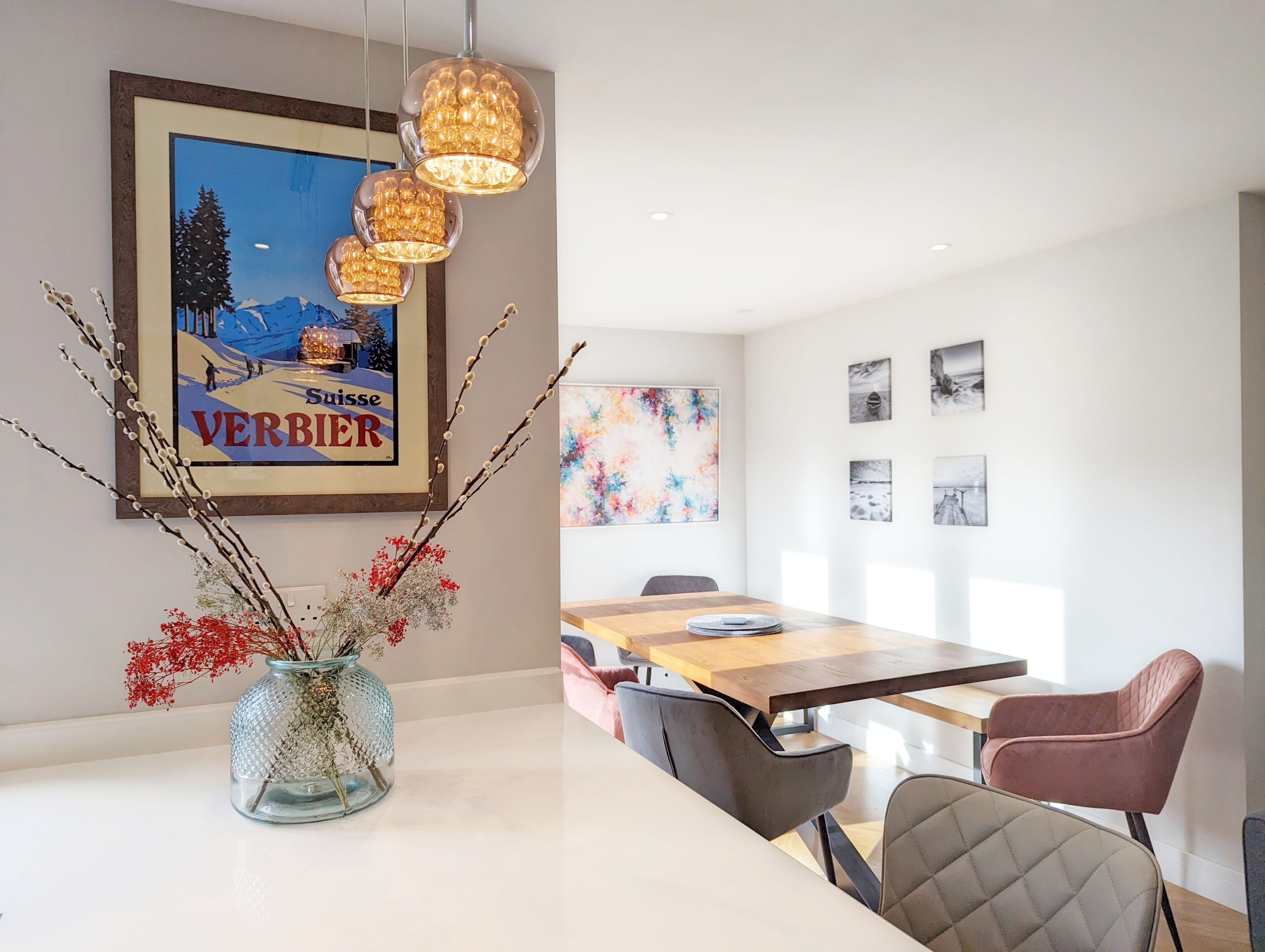 Un espace repas moderne avec une table en bois, des chaises et un vase décoré de branches et de fleurs.