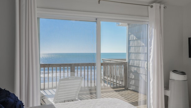 A bedroom with a large sliding glass door leading to a balcony with a view of the ocean. - Topsail Pearl #132 – Oceanfront Retreat with Beach Access & Sound Views (North Topsail Beach)