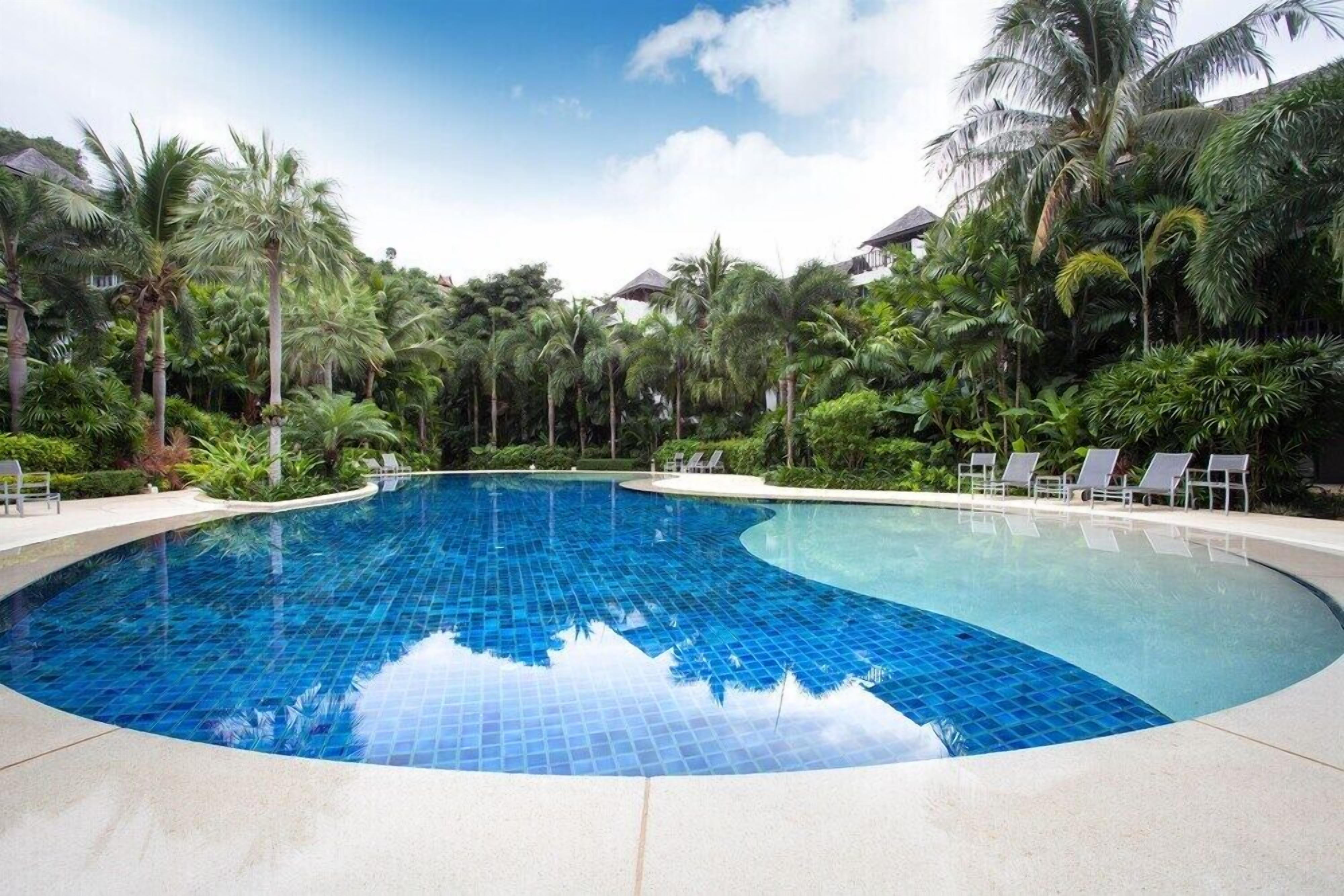 A large, clear blue swimming pool surrounded by palm trees and lounge chairs.
