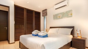 A neatly made bed with a white comforter, a bedside lamp, and a folded towel on the nightstand.
