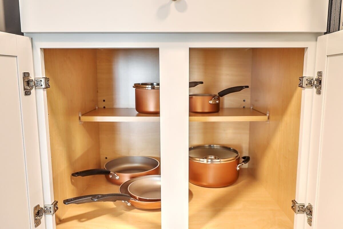 A kitchen cabinet with two shelves, each holding a copper pot and a pan.