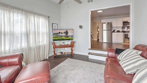 A living room with a TV, leather chairs, a glass coffee table, and a ceiling fan. - Quiet Comfort  Chas Attractions- Family Friendly (Goose Creek)