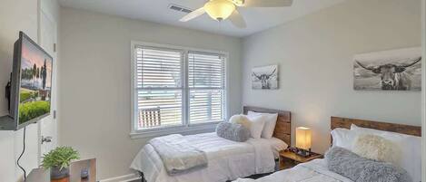 Une chambre avec deux lits, un ventilateur de plafond, une télévision et une fenêtre avec des stores.