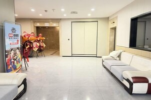 Un vestíbulo de hotel con una recepción, un sofá, un televisor en la pared y una puerta que da a otra habitación.