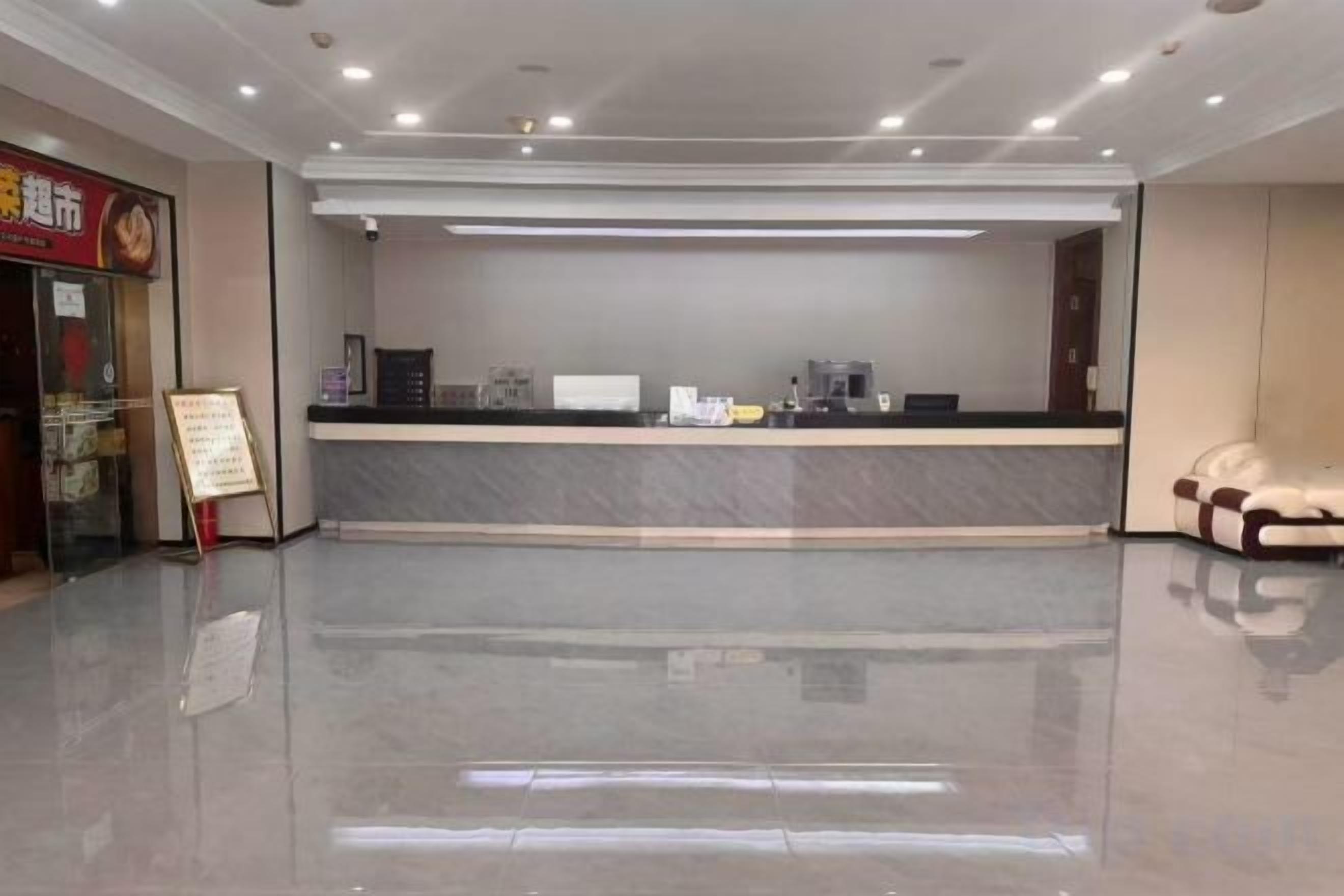 Zona de recepción de un hotel con mostrador de mármol, pantalla digital y un área de descanso con sofá.