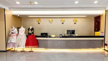 Zona de recepción de un hotel con suelo de mármol, mostrador de recepción y dos maniquíes vestidos con traje tradicional.