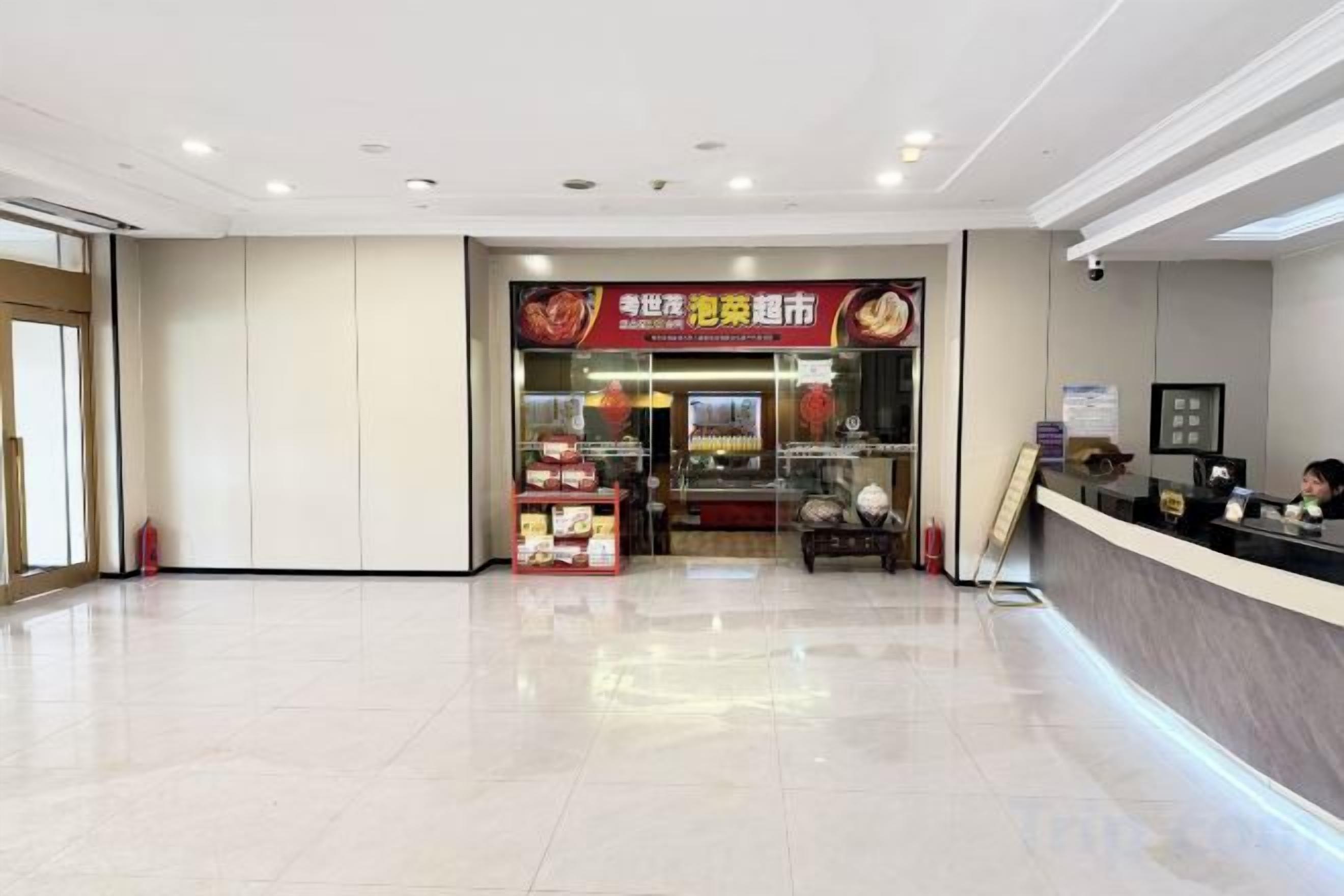 A hotel lobby with a reception desk, a food counter, and a tiled floor.