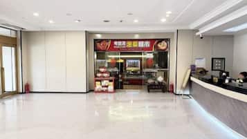 A hotel lobby with a reception desk, a food counter, and a tiled floor.