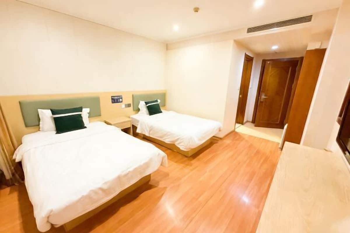 Habitación de hotel con dos camas, suelo de madera y una puerta que da a otra habitación.