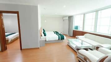A modern hotel room with a bed, a sofa, a glass coffee table, and a large window.