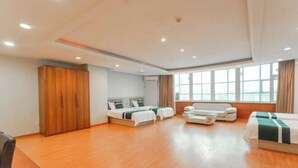 A hotel room with a wooden floor, a bed, a sofa, a small table, and a window with curtains. - Kocemo Hotel (Yanji)