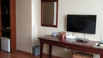 A hotel room with a wooden desk, a television, a small trash bin, and a cabinet with a mirror.