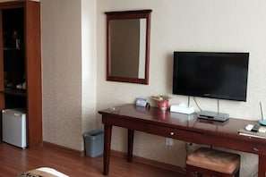 A hotel room with a wooden desk, a television, a small trash bin, and a cabinet with a mirror. - Kocemo Hotel (Yanji)