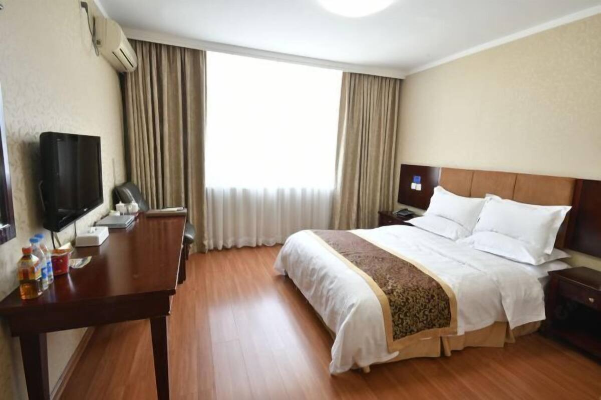 Habitación de hotel con cama, escritorio, televisión y ventana con cortinas.