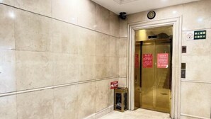 A marble-floored hallway with an elevator door, a sign indicating a 24-hour service area, and a fire safety sign. - Kocemo Hotel (Yanji)