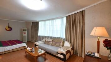 A hotel room with a sofa, a wooden coffee table, a lamp, and a bed with a colorful blanket.