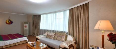 A hotel room with a sofa, a wooden coffee table, a lamp, and a bed with a colorful blanket.