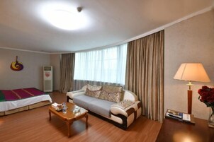 A hotel room with a sofa, a wooden coffee table, a lamp, and a bed with a colorful blanket.