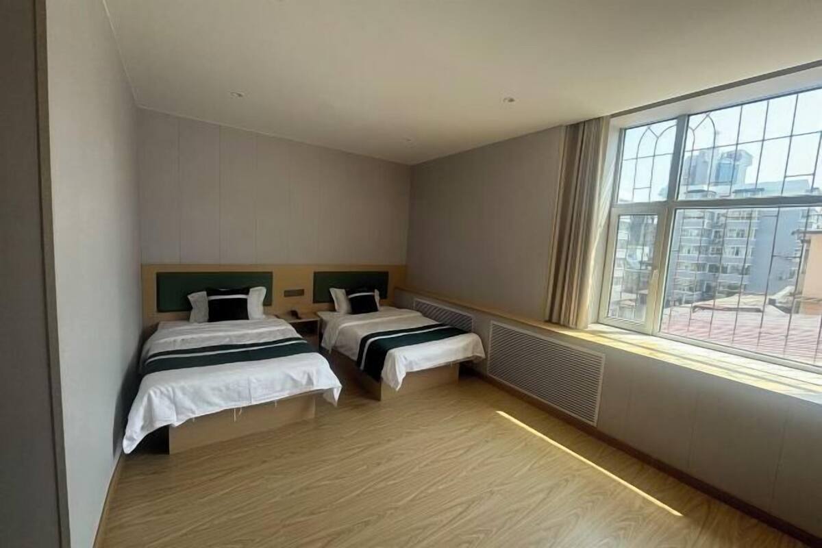 Habitación de hotel con dos camas, un ventanal grande y vistas a la ciudad.