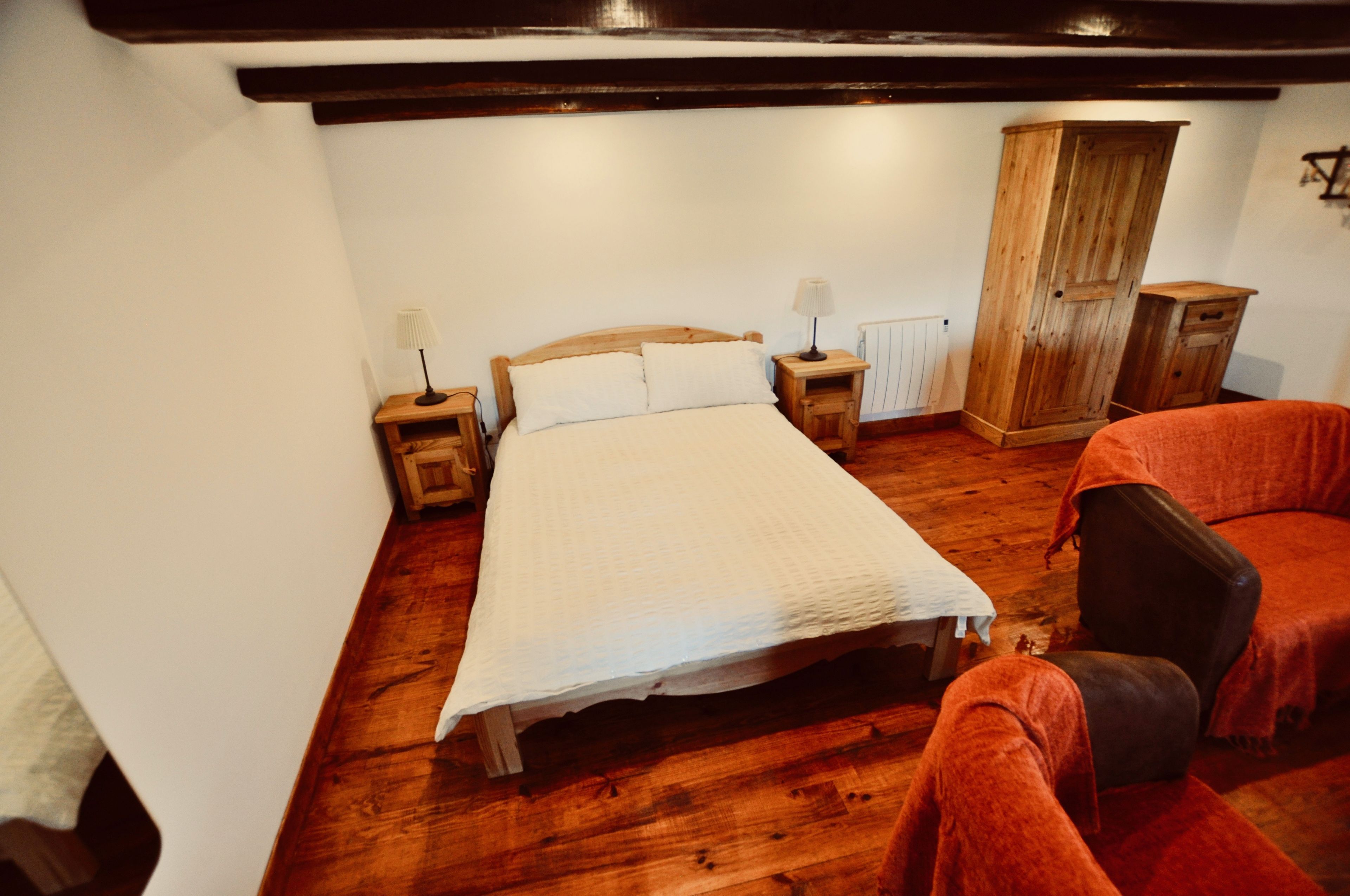 A bedroom with a wooden bed, two bedside tables with lamps, a wooden wardrobe, and a red armchair.