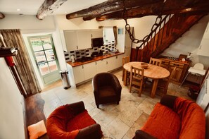 Uma sala de estar aconchegante com lareira, uma área de jantar com mesa e cadeiras de madeira, e uma cozinha com armários brancos e escada de madeira.
