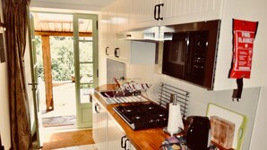 Eine Küche mit weißen Schränken, einem Herd und einer Mikrowelle. Ein Fenster mit Vorhängen und eine Tür, die nach draußen führt.
