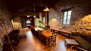 Un coin repas rustique avec une longue table et des chaises en bois, des murs en pierre et des lampes suspendues.
