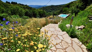 Un chemin de pierre mène à une piscine entourée d’une végétation luxuriante et de fleurs aux couleurs vives.