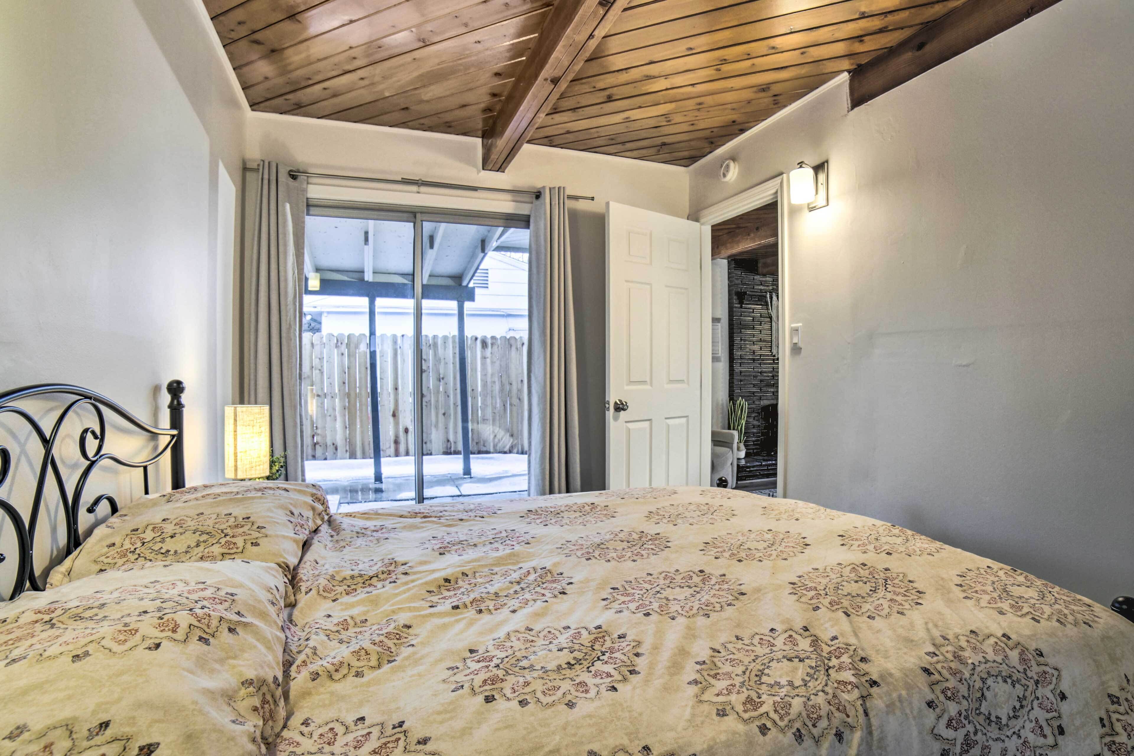 Une chambre avec un grand lit, un plafond en bois, une porte-fen être coulissante donnant sur l’extérieur et une porte blanche menant à un placard.