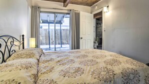 Een slaapkamer met een groot bed, een houten plafond, een glazen schuifdeur naar buiten en een witte deur naar een kast.