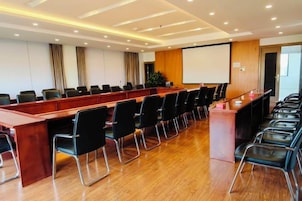 Un salón de conferencias con una larga mesa, sillas, una pantalla de proyector y una pizarra.