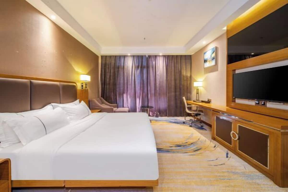 Quarto de hotel com uma cama grande, uma escrivaninha com cadeira, uma televisão e uma cortina.