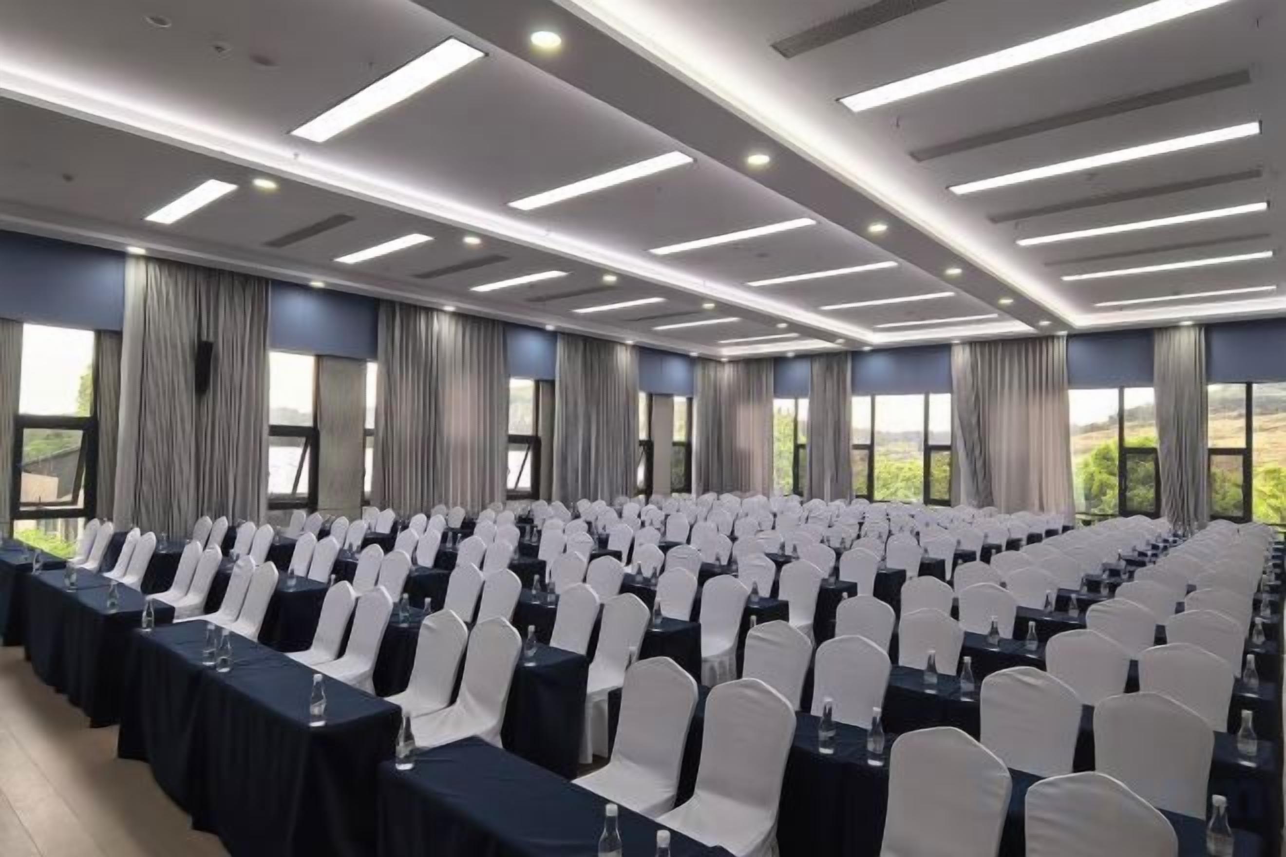 A conference room with rows of tables and chairs, large windows, and a modern ceiling design.