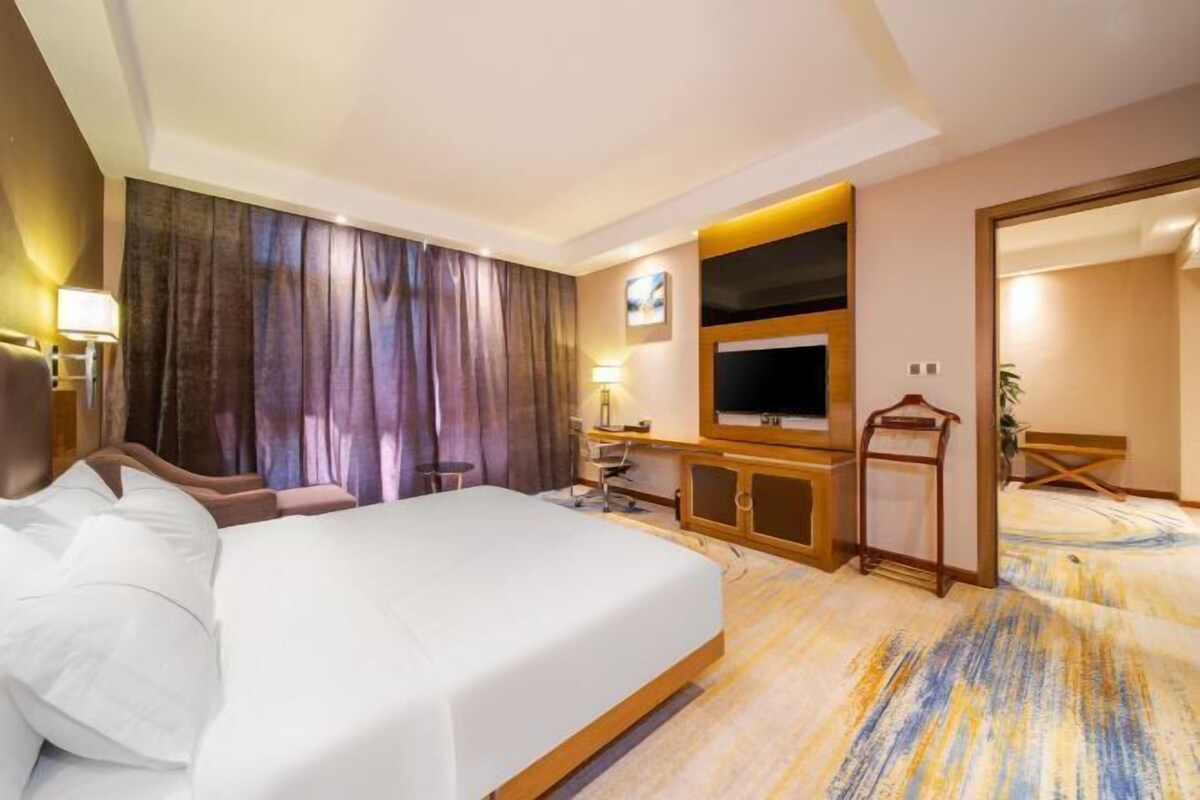 A hotel room with a large bed, a desk with a chair, a television, and a mirror.