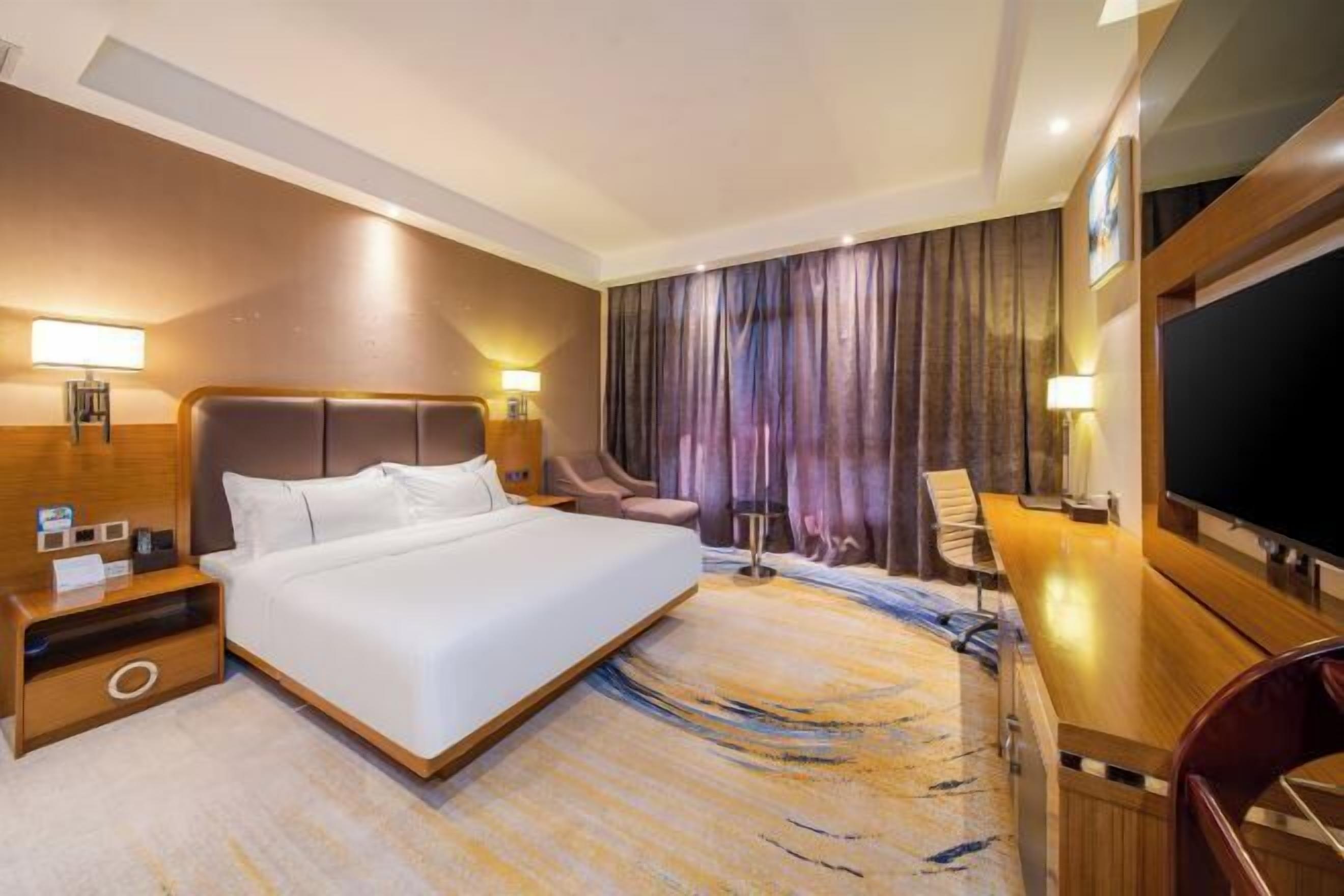 Una habitación de hotel con una cama grande, un escritorio, una silla, un televisor y una cortina.