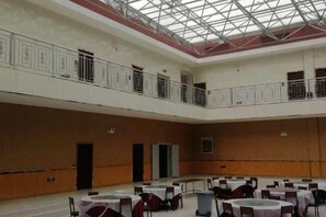 Un amplio salón interior con techo alto, varias mesas y sillas, y un balcón en el nivel superior.